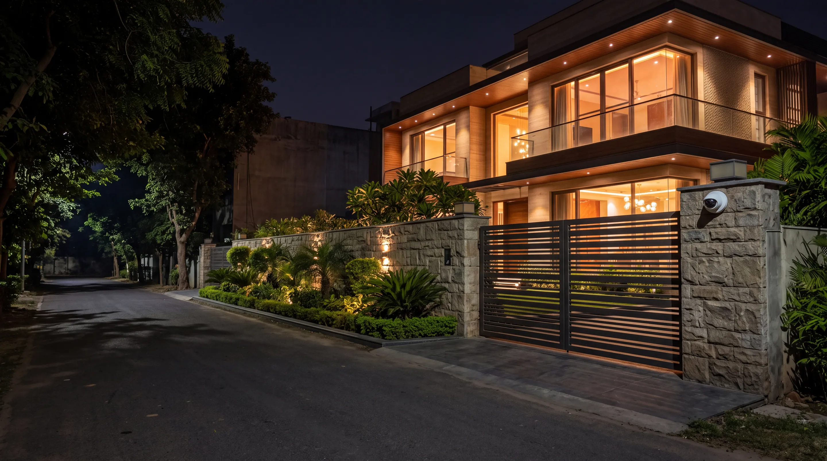 A two-storey villa at night behind a steel gate, with a camera on the gate pillar